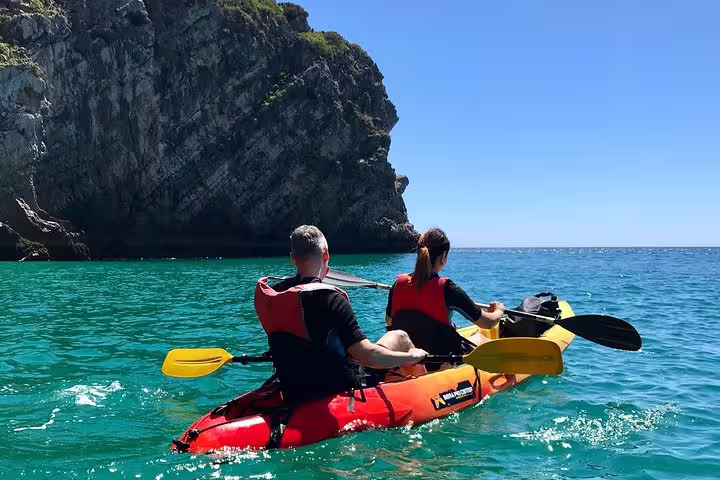 Two kayakers paddle through the crystal-clear waters of Sesimbra, exploring the stunning cliffs of Arrábida Natural Park.