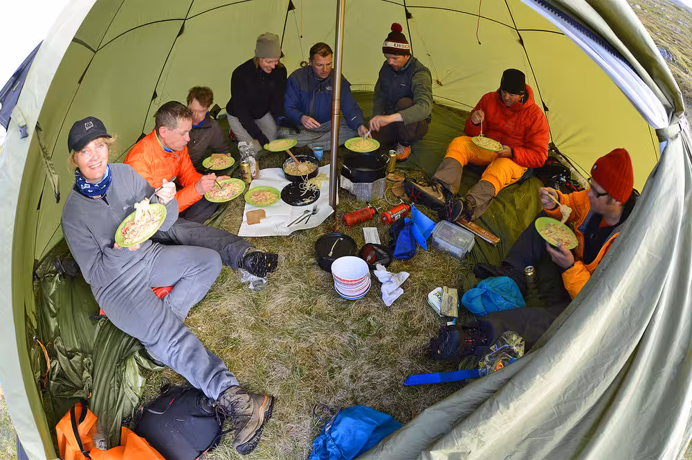 Kayak expedition group eating hot camp meal inside tent, Paddle in the Wild multi-day wilderness adventure