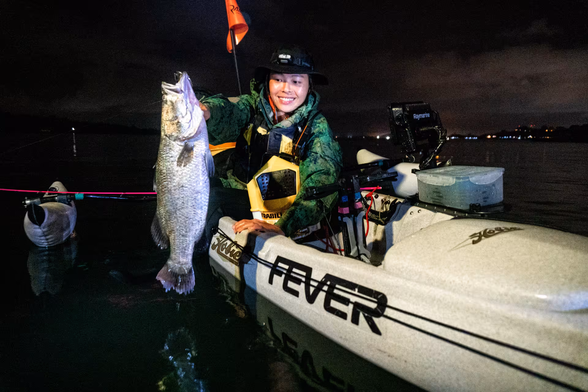 Kayaker in green jacket proudly displays a large catch during night fishing tour at Pulau Ubin.