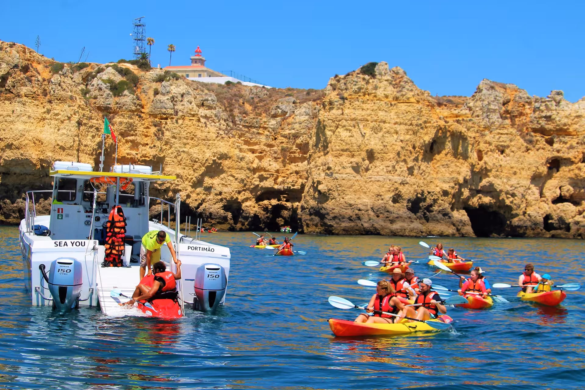 Group kayaking tour in Lagos, Algarve, paddling past golden sea cliffs and caves with support boat on clear blue water