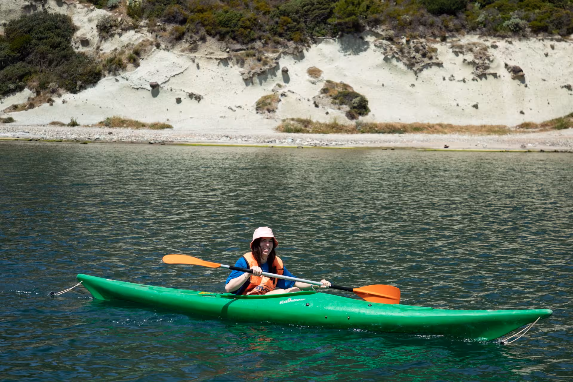 Smiling kayaker in a green kayak on the scenic Temo River, Bosa, enjoying a sunny day adventure.