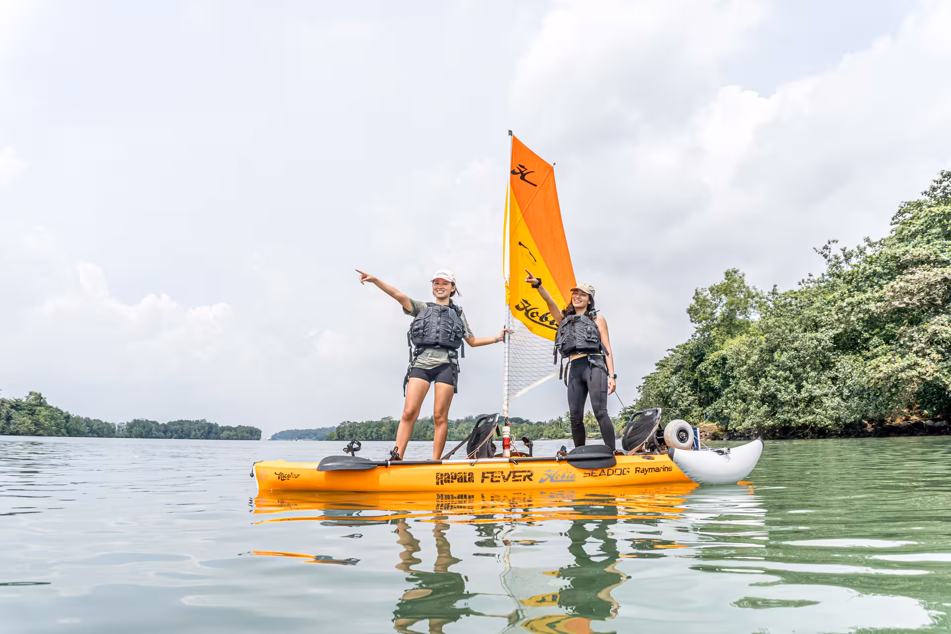 Two explorers standing on a kayak, pointing towards the scenic horizon during a sailing adventure.