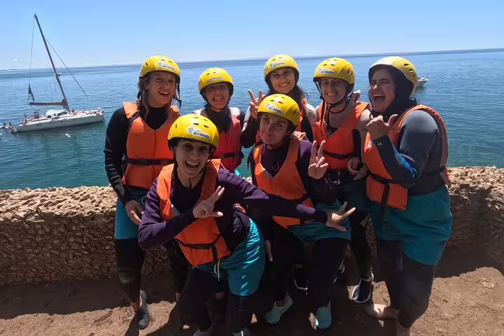 Group of happy kayakers in wetsuits and helmets pose by the Lisbon coast, ready for a kayaking and snorkeling adventure.