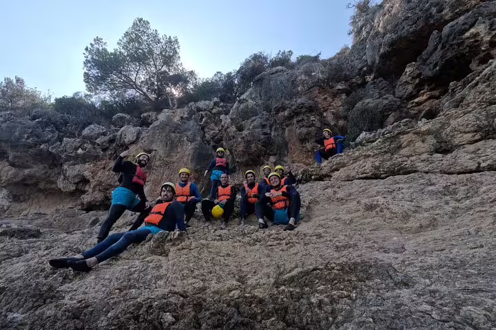 Group of adventurers in life jackets and helmets posing on rugged cliffs during a kayak and snorkeling tour in Lisbon.