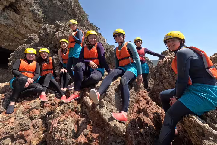 Group of adventurers in safety gear enjoying a sunny day of kayak and snorkeling exploration on rocky cliffs in Lisbon.