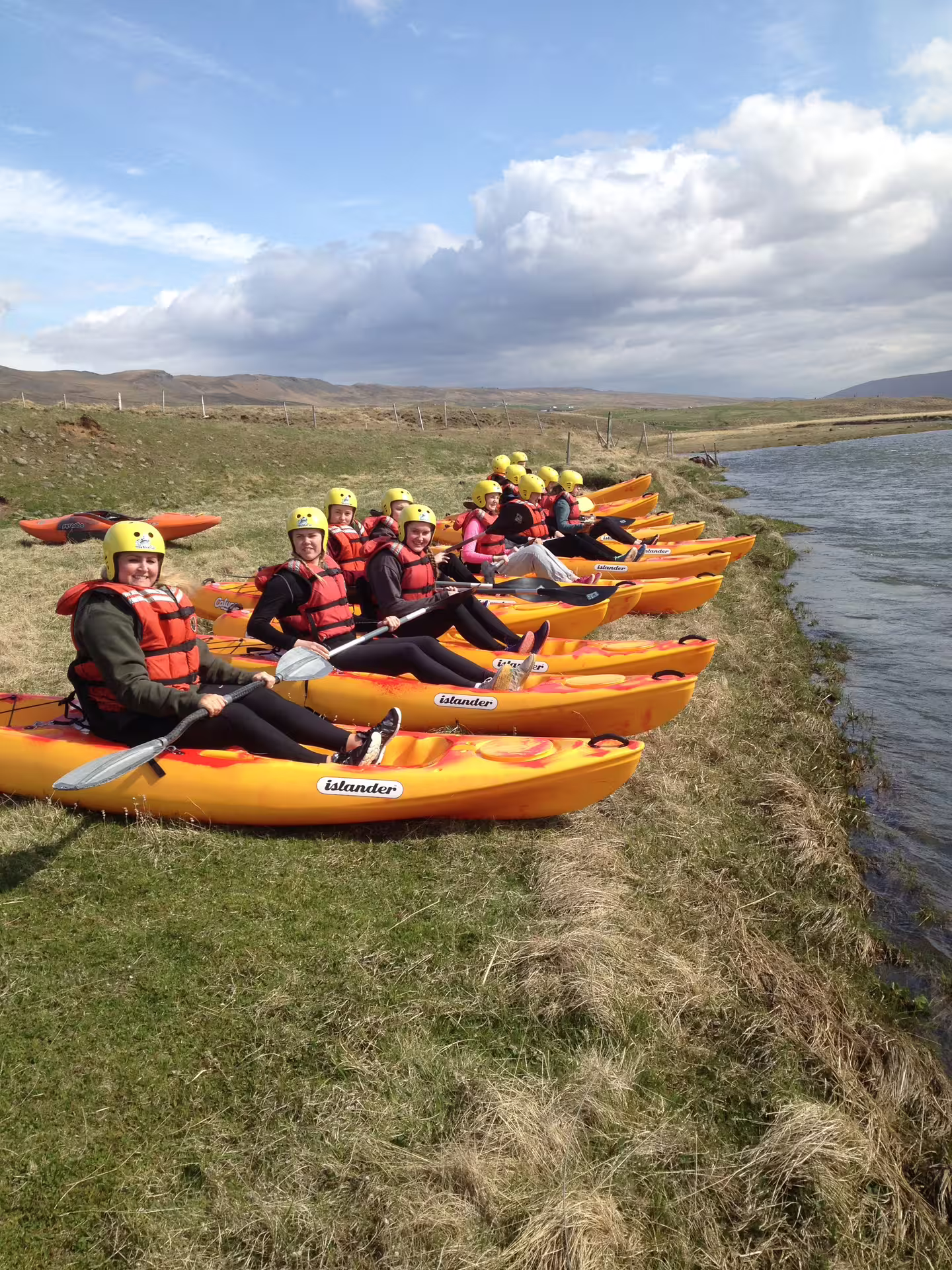 Group of kayakers in bright gear ready to launch on the scenic Svartá River, Iceland, under a clear blue sky.