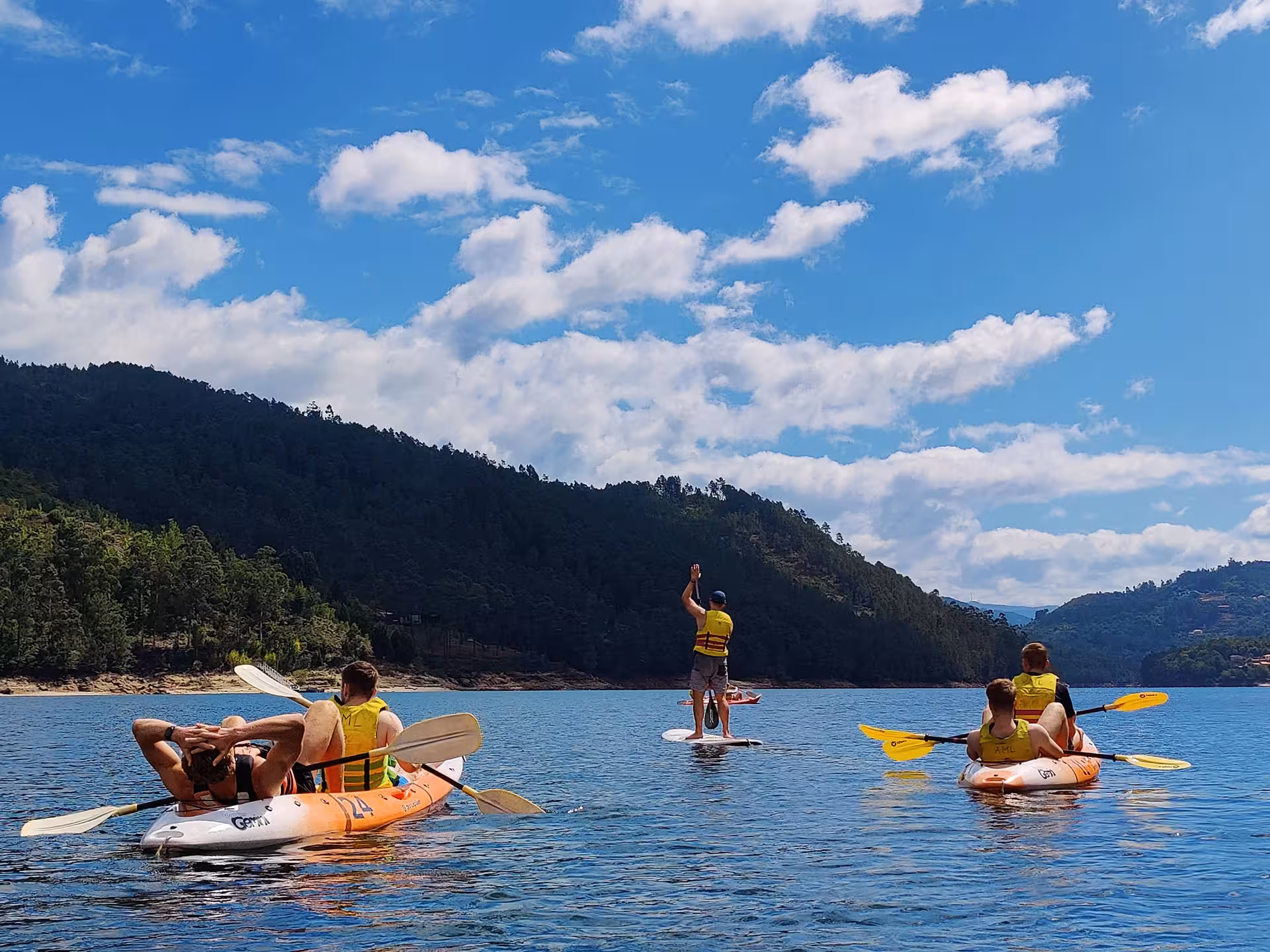 Kayakers and paddleboarder explore tranquil waters of Peneda Geres National Park under a bright blue sky.