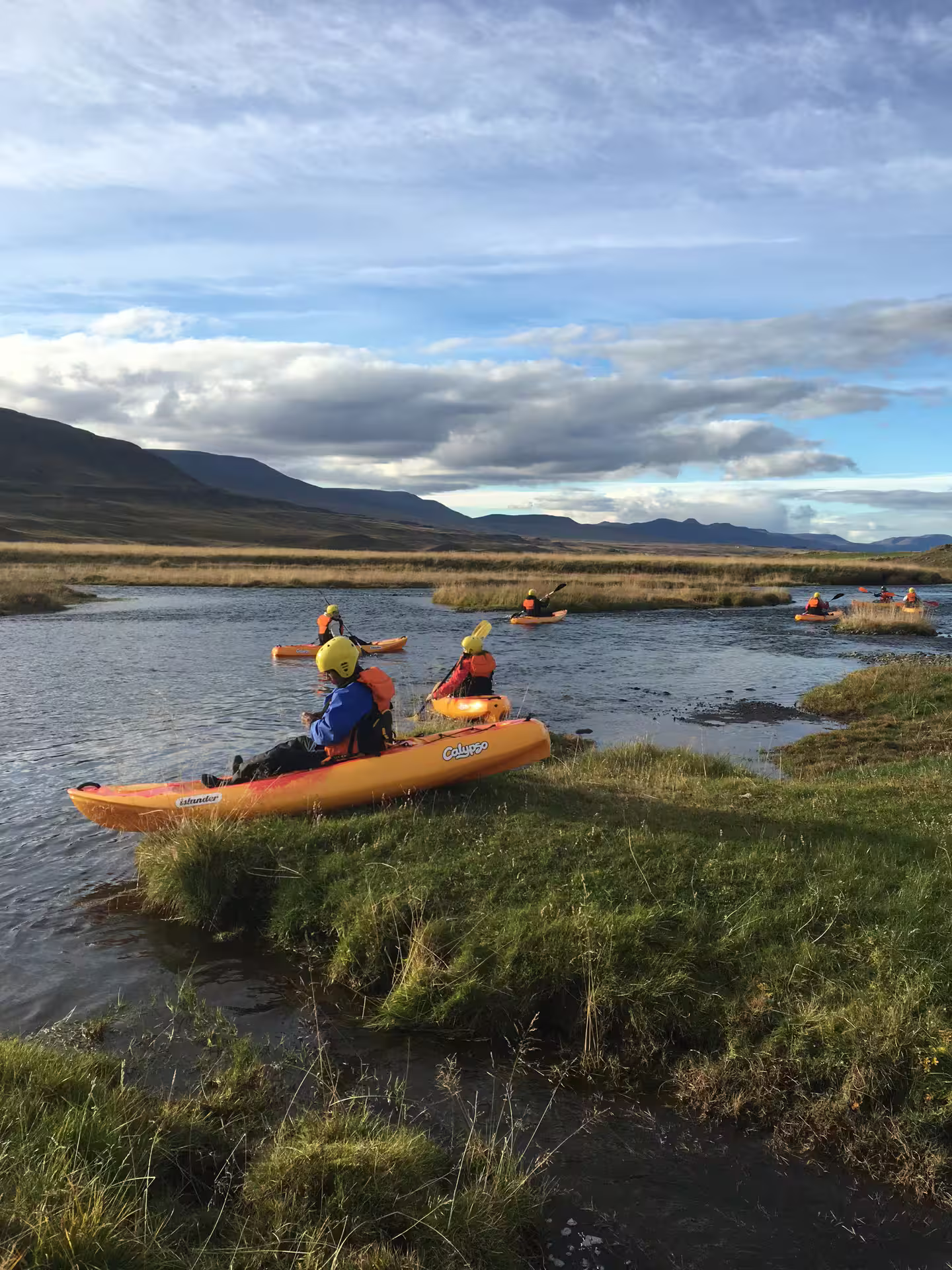 Kayakers paddle on the scenic Svartá River, surrounded by lush greenery and dramatic Icelandic landscapes under a vibrant sky.