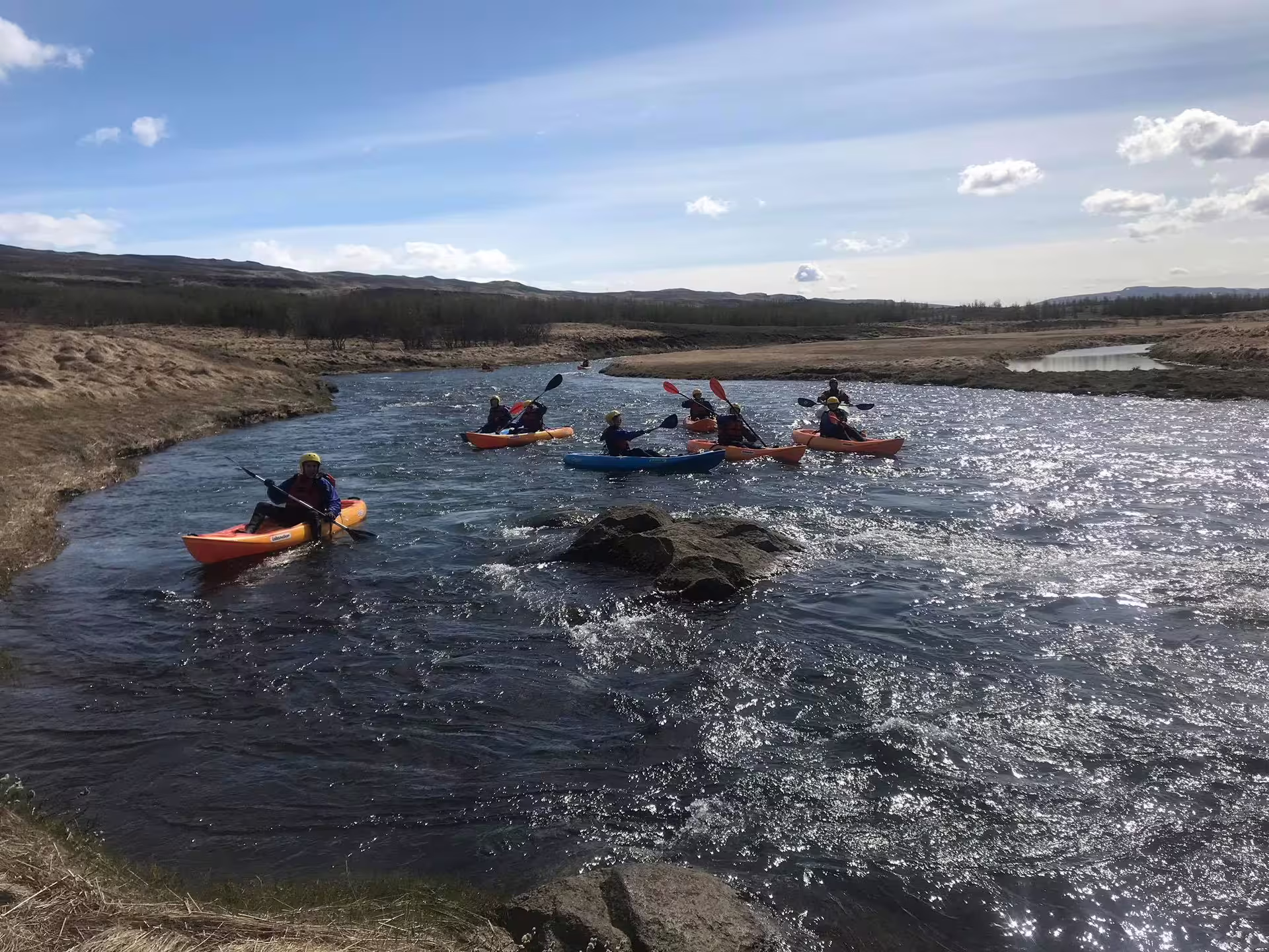 Kayakers paddle through the scenic Svartá River under a clear sky, offering an adventurous Icelandic nature experience.