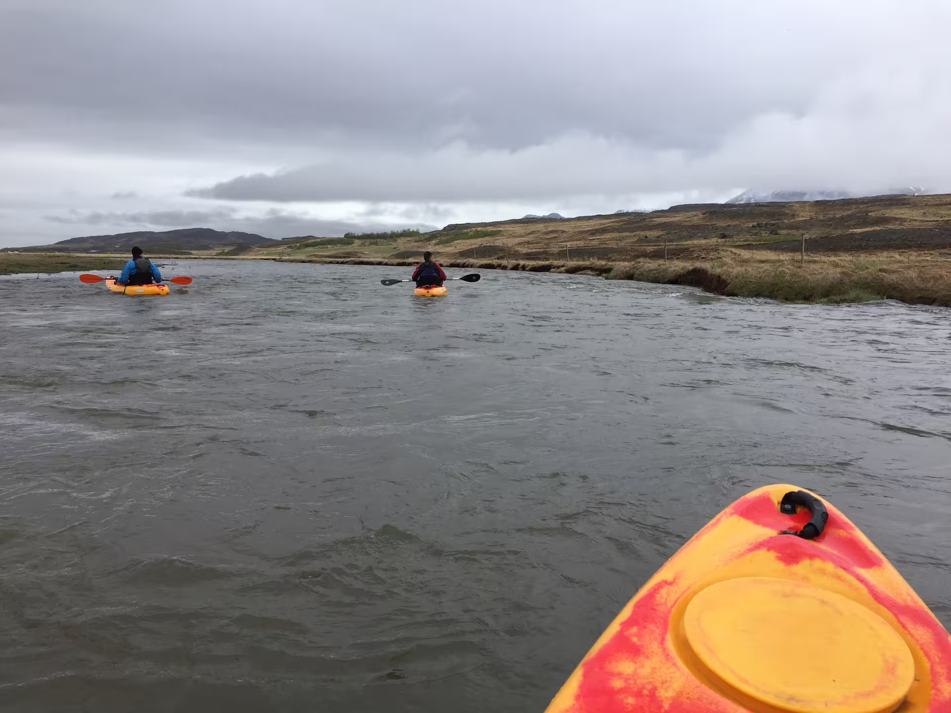 Kayakers navigate the scenic Svartá River in Iceland, surrounded by lush landscapes and overcast skies, ideal for adventure seekers.
