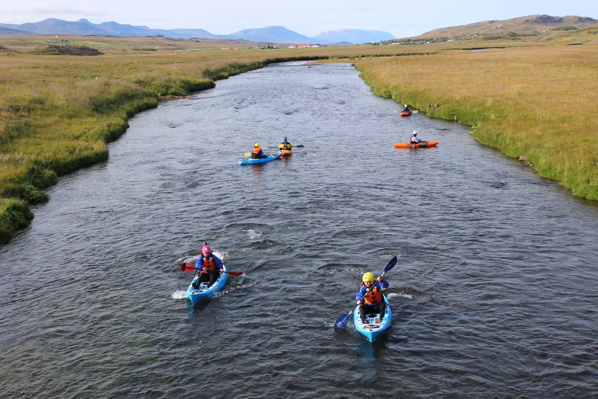 Kayakers navigate the scenic Svartá River, surrounded by lush landscapes and distant mountains, ideal for adventure seekers in Iceland.