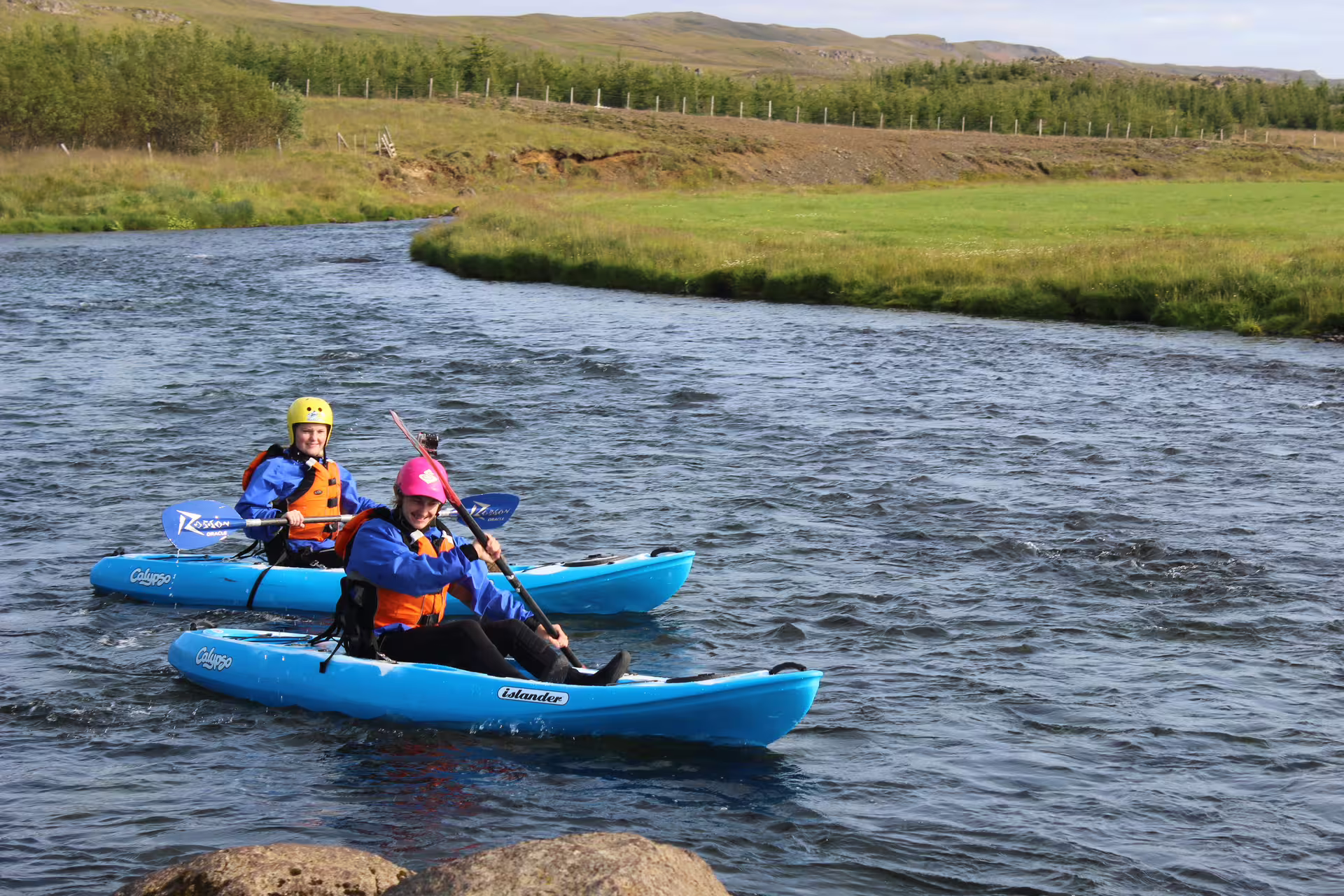 Kayakers enjoy a sunny adventure on the scenic Svartá River, navigating gentle rapids surrounded by lush greenery.