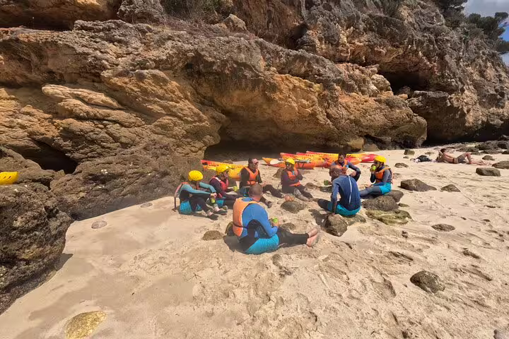 Group of kayakers in wetsuits and helmets resting on a rocky beach during a Lisbon kayaking and snorkeling adventure tour.