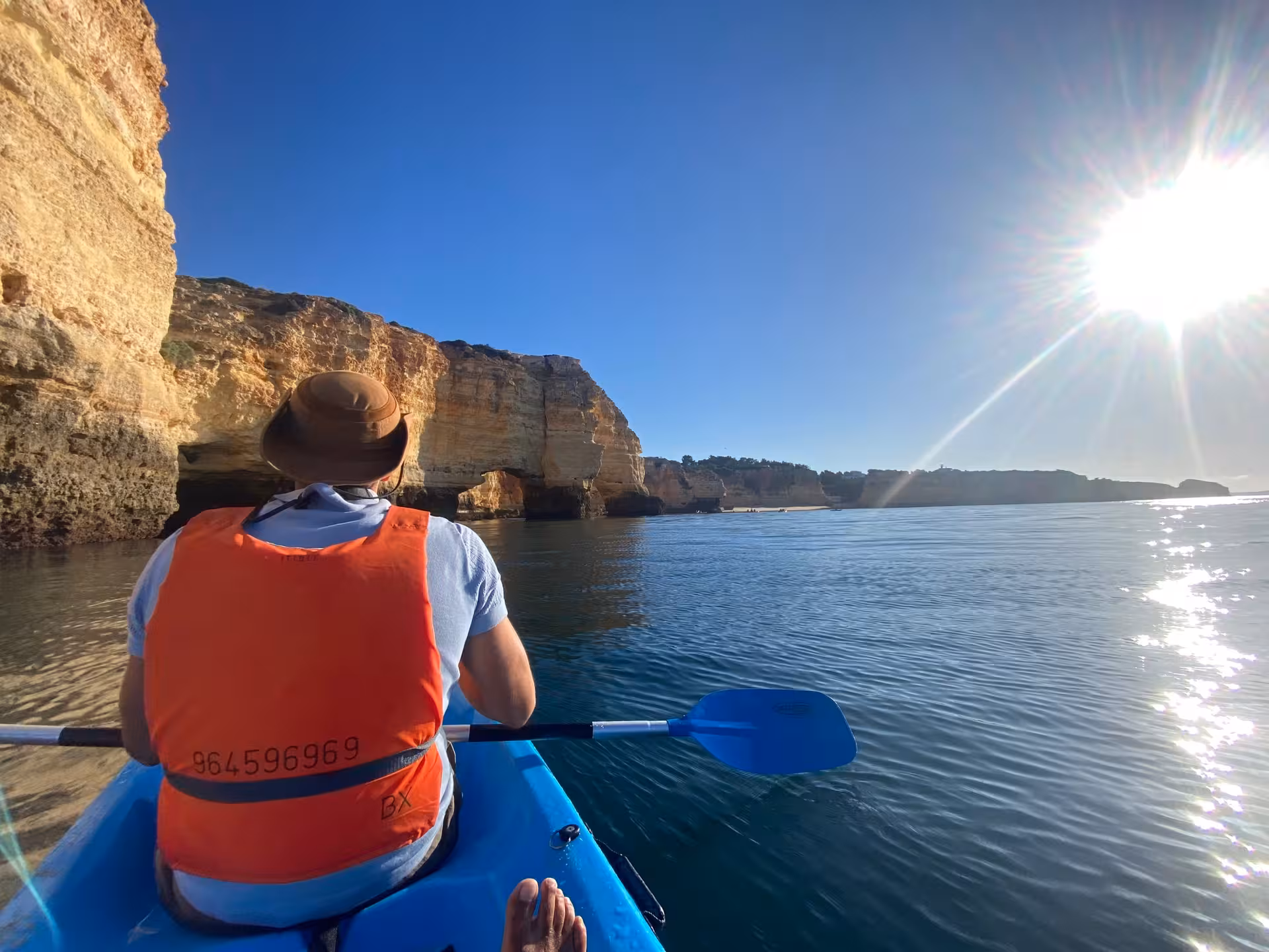 Kayaker in orange vest paddles at sunrise along Benagil’s dramatic Algarve cliffs toward hidden sea caves on a peaceful Atlantic sea