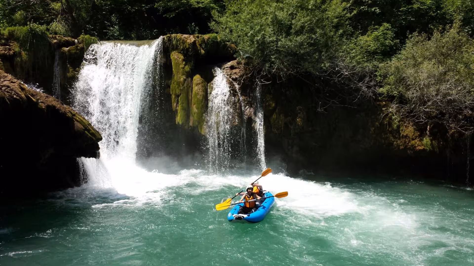Kayakers navigating the rapids near a stunning waterfall in Mreznica Canyon, Croatia, under a bright, sunny sky.