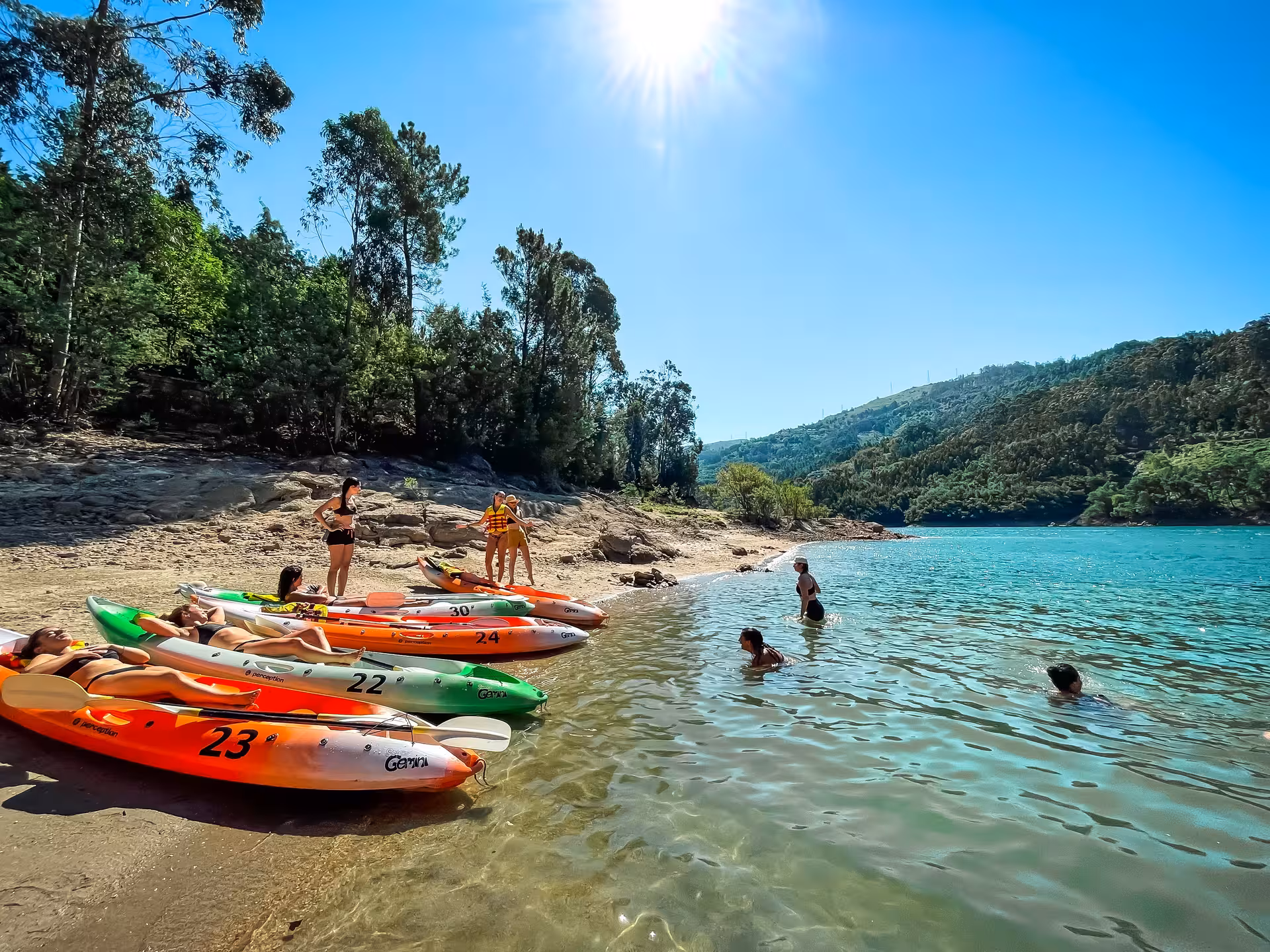 Kayakers enjoy a sunny day on the clear waters of Peneda Geres National Park, surrounded by lush green hills.