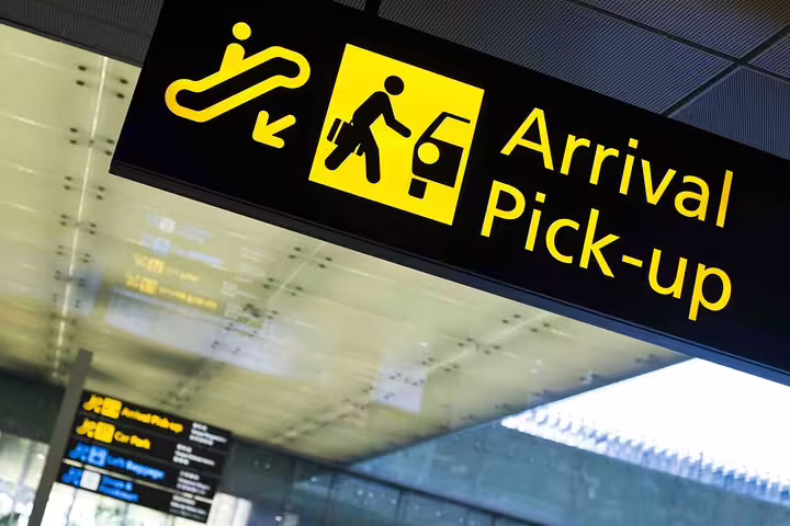 Airport arrival pick-up sign with yellow icons showing escalator and passenger loading a vehicle