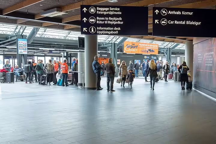 Keflavik Airport arrivals hall with travelers and signs for buses to Reykjavik and baggage service