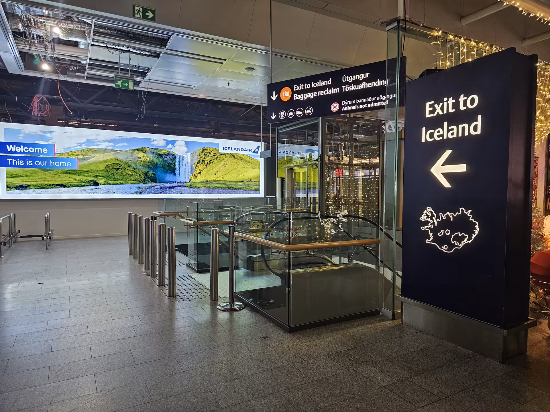 Exit to Iceland sign at Keflavik Airport arrivals hall with escalators and Icelandair welcome display