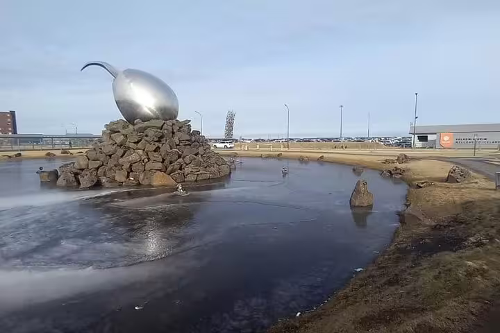 Shiny silver egg sculpture on rock pile near Keflavik Airport Iceland with frozen pond