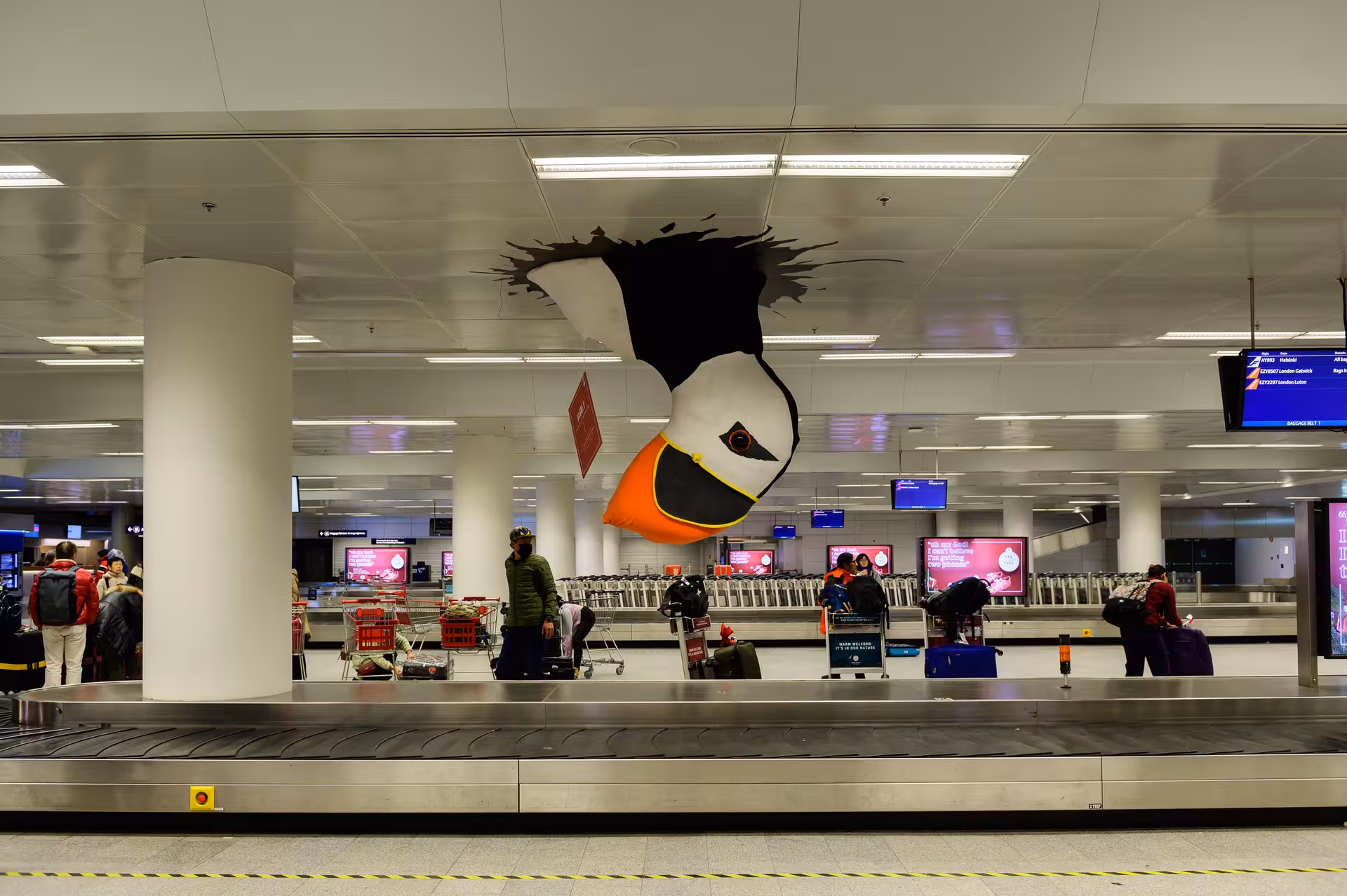 Keflavik Airport KEF baggage claim hall with puffin mascot decoration and passengers waiting