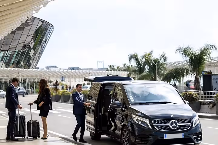 Chauffeur opening door of black Mercedes luxury van for two passengers with luggage at airport