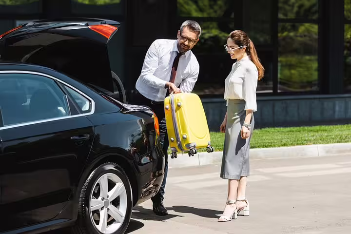 Man loading yellow suitcase into black car trunk for private airport transfer