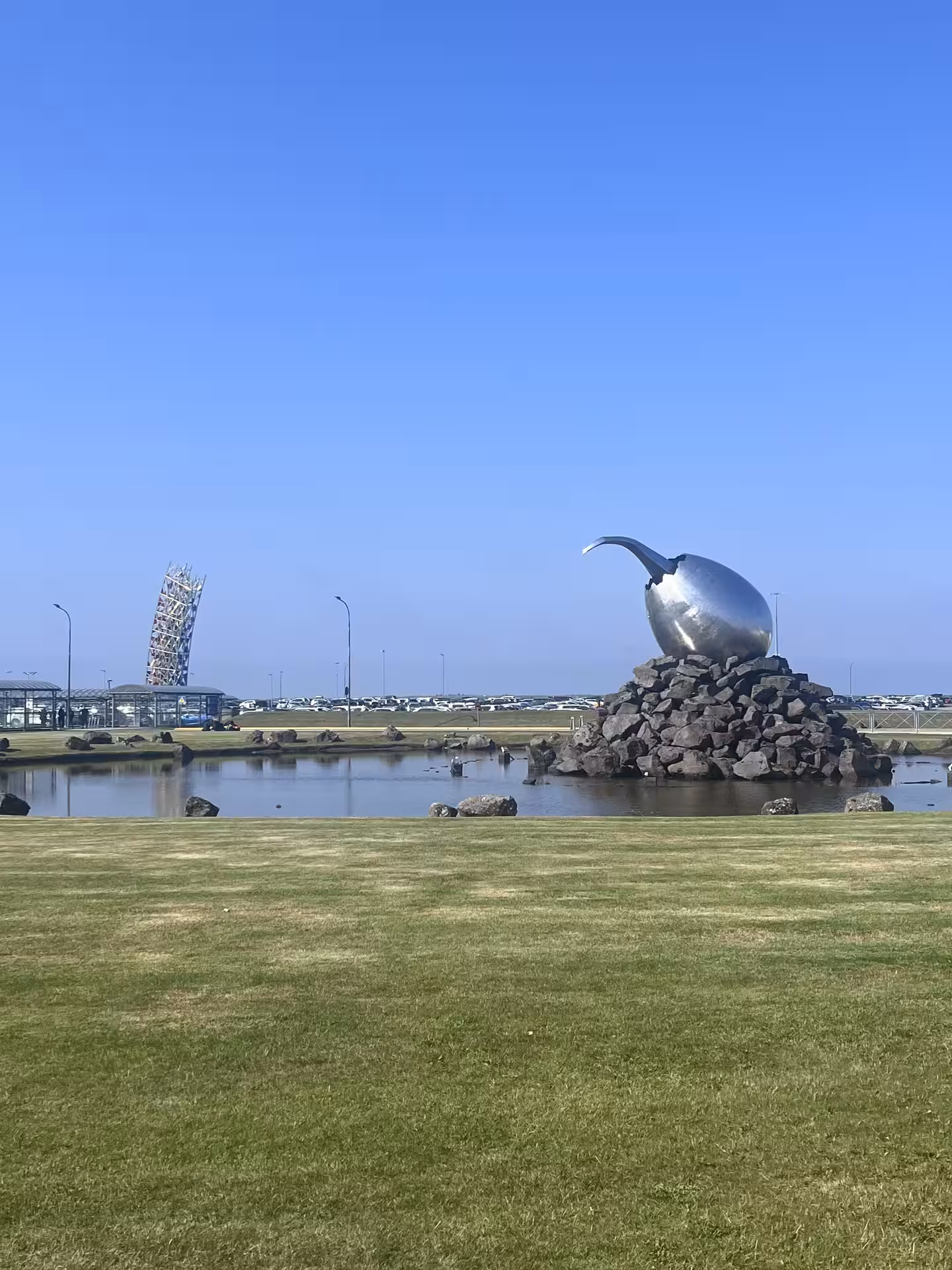Keflavík Airport exterior with Iceland landmark sculpture by pond, meeting point for private transfer to Reykjavik