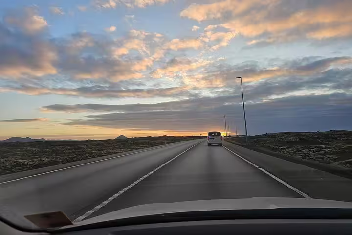 View from car dashboard driving toward Reykjavik at sunset on open Icelandic highway