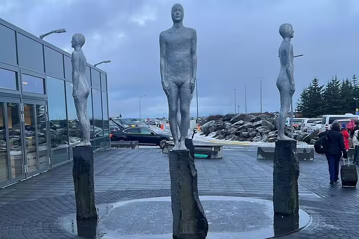 Three tall human sculptures on stone pillars outside Keflavik Airport terminal, Iceland