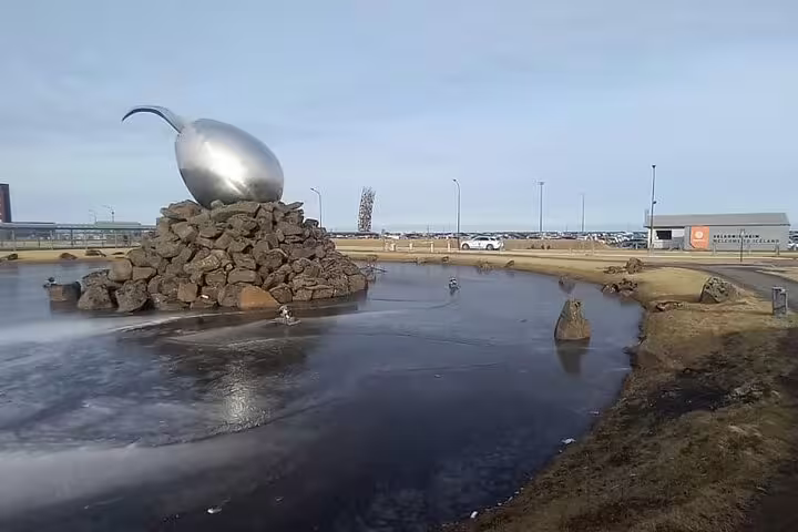 Silver egg sculpture on rock pile near Keflavik Airport with frozen pond in foreground