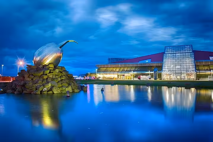 Keflavik Airport terminal at blue hour with large metallic egg sculpture reflected in water