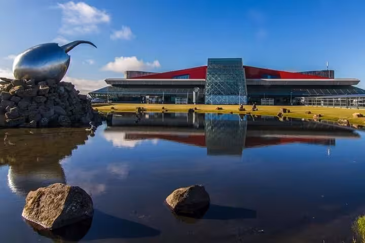 Keflavik International Airport terminal with red roof, glass facade, and reflective pond in foreground