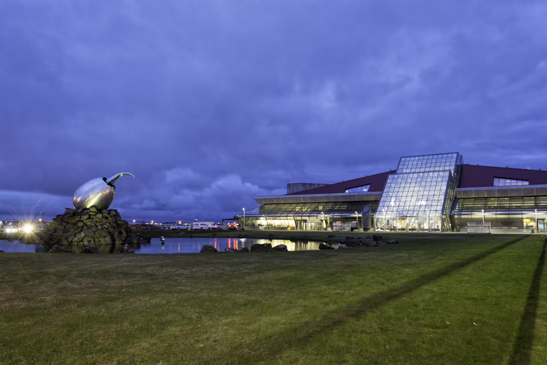 Keflavik International Airport terminal at dusk with metallic sculpture and illuminated glass facade
