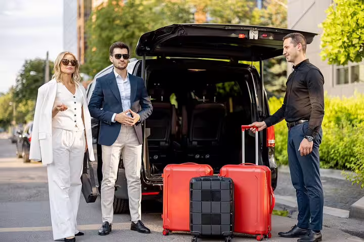 Chauffeur loading red luggage into black luxury van for airport transfer service