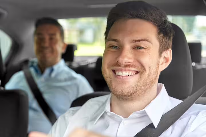 Smiling driver in white shirt with passenger in backseat during airport transfer