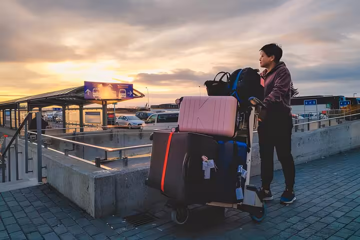 Traveler with luggage cart at Keflavik Airport during sunset, ready for transfer to Reykjavik