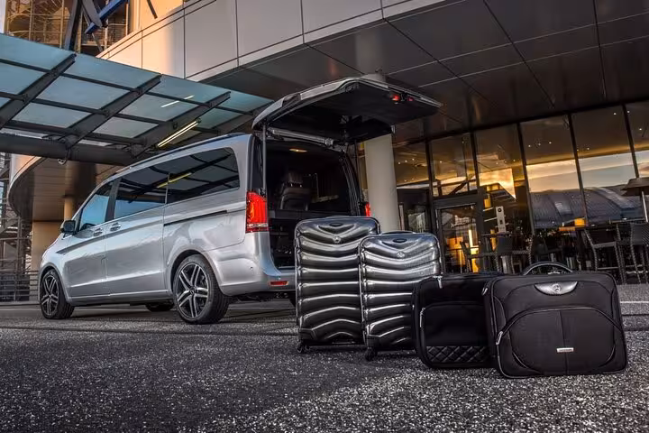 Silver Mercedes van with open trunk and black luggage outside hotel for Keflavik Airport transfer