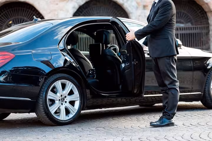 Chauffeur in black suit opening door of black Mercedes sedan on cobblestone street