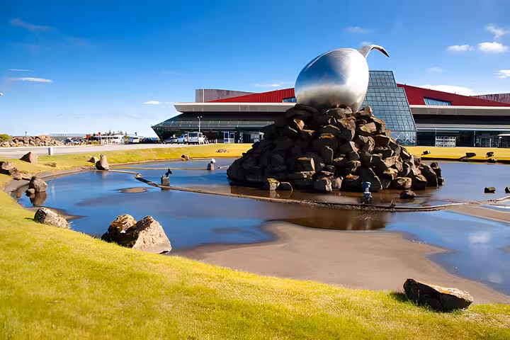 Keflavik Airport terminal building with large silver sphere sculpture on rock pile beside reflective pond