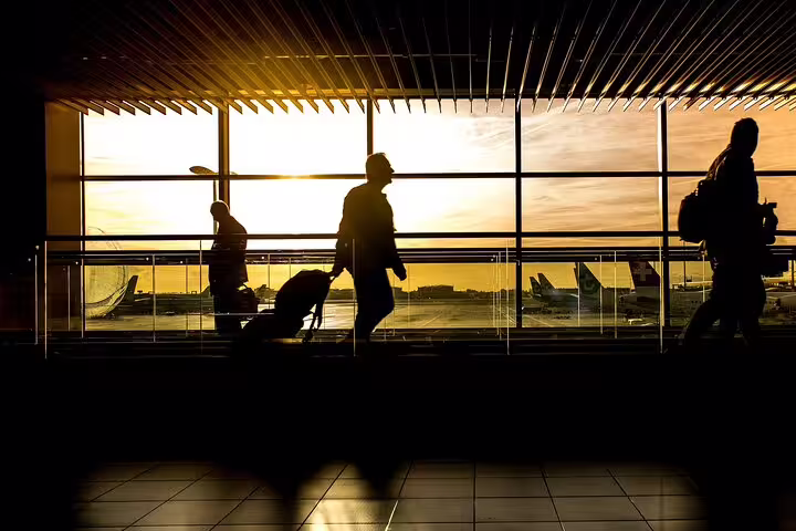 Travelers with luggage walking through airport terminal at sunset with planes visible outside