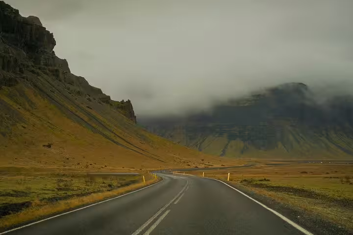 Two-lane road winding through Iceland's dramatic volcanic mountains under stormy skies near Keflavik