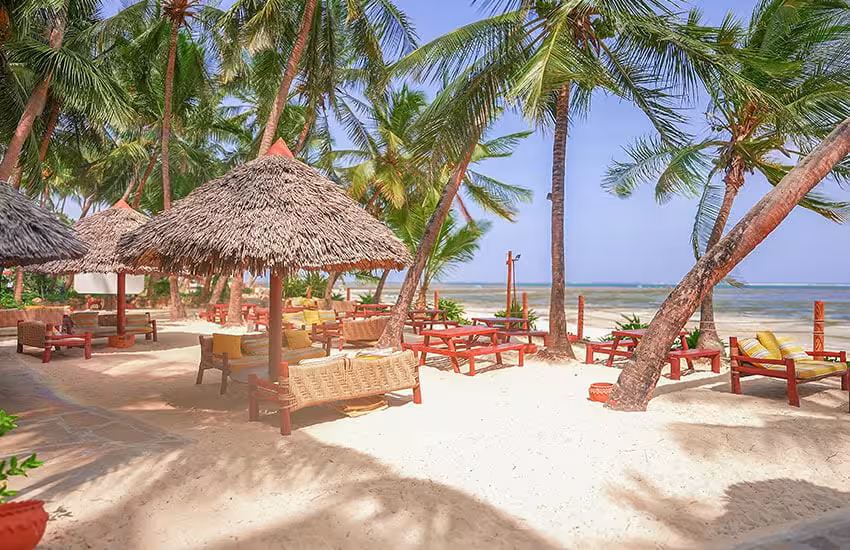 Beachfront dining area with thatched umbrellas and palm trees at a Kenya Coast golf tour resort