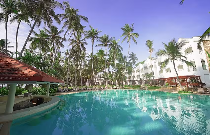 Luxury resort pool surrounded by palm trees under a clear blue sky on Kenya's coastline.