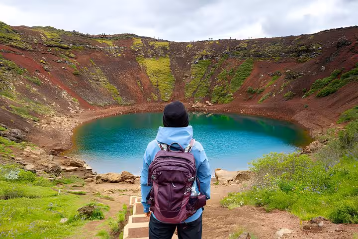 Hiker with purple backpack overlooking turquoise Kerid volcanic crater lake on Golden Circle tour