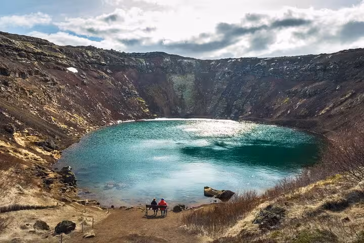Two visitors sitting by the turquoise volcanic crater lake Kerid on Iceland's Golden Circle route
