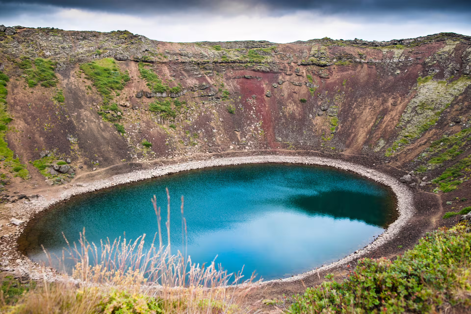 Kerid volcanic crater lake with vivid turquoise water surrounded by red and green slopes, Iceland