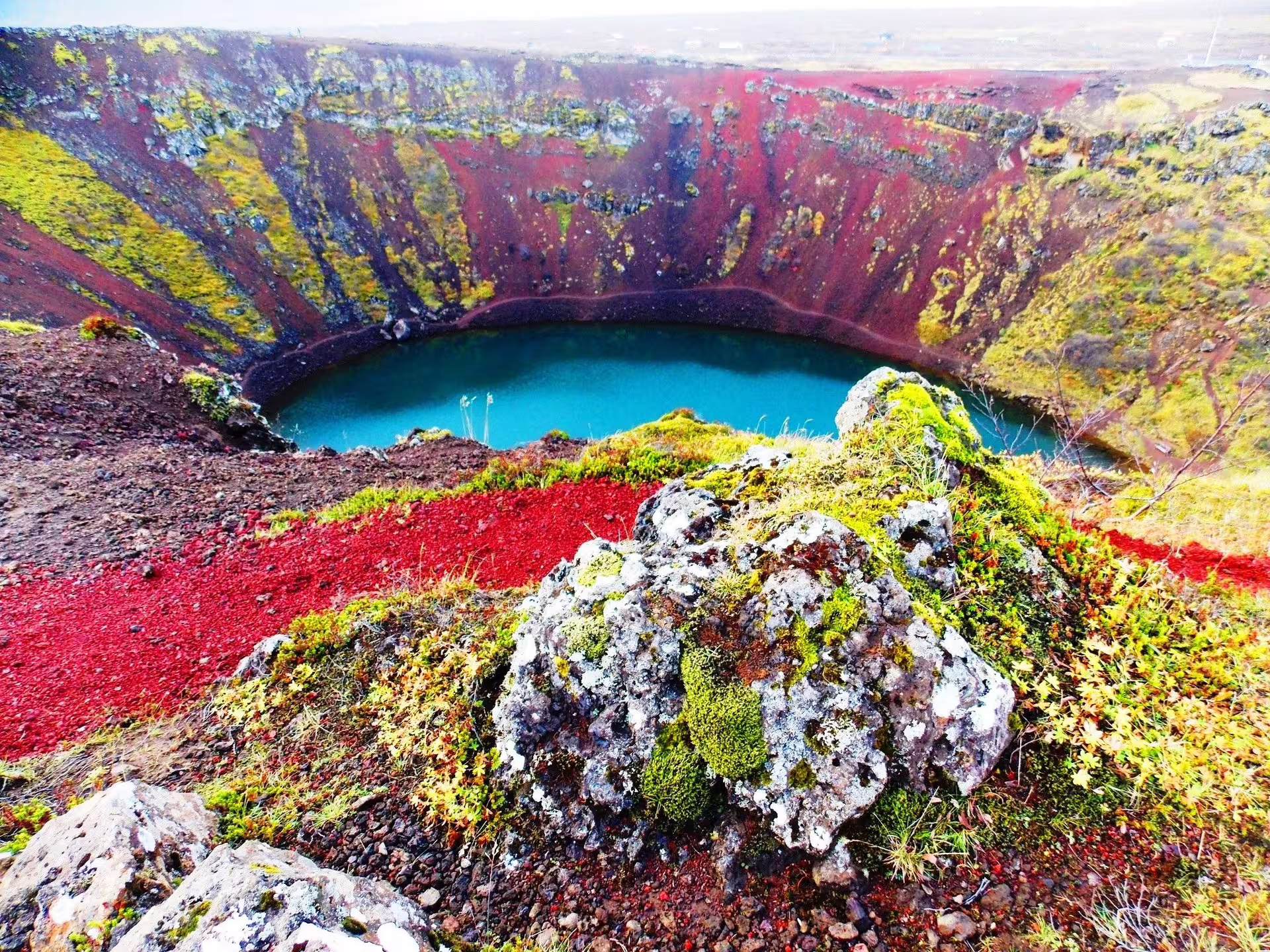 Kerid volcanic crater lake with turquoise water, red lava rocks and moss in Iceland's Golden Circle