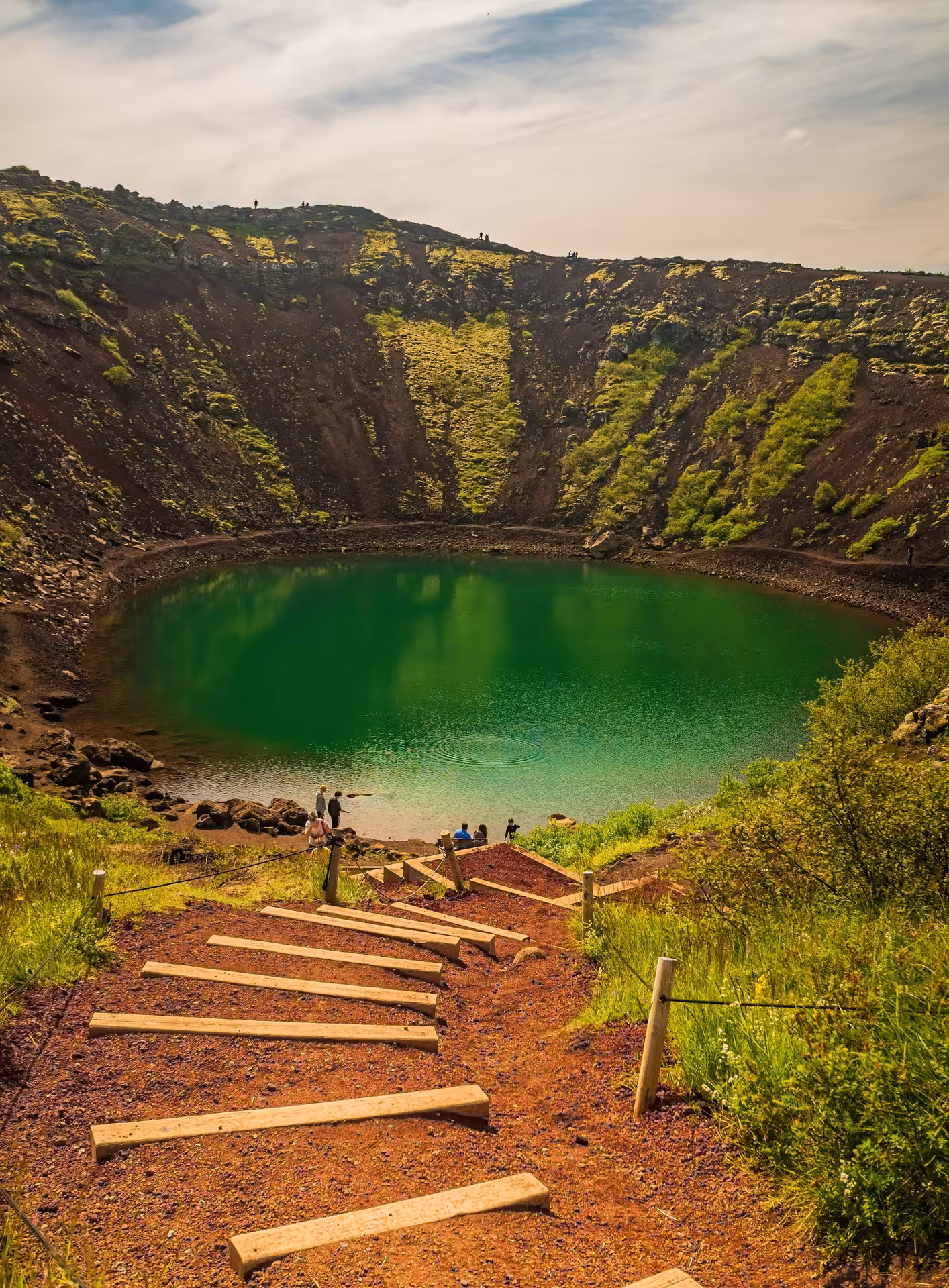 Kerid volcanic crater lake with vivid green water and wooden steps leading down in Iceland