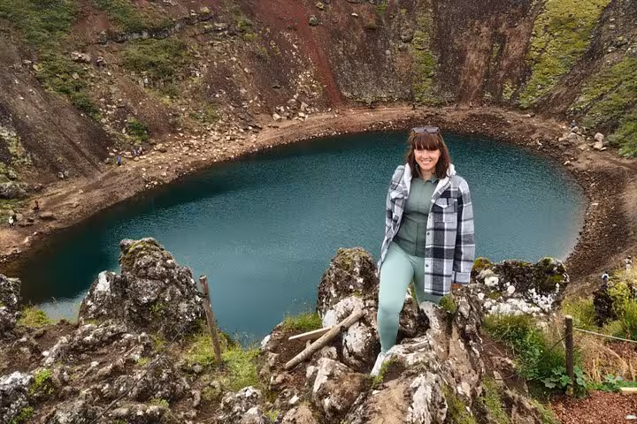 Woman standing on volcanic rocks above turquoise Kerid Crater Lake on Iceland Golden Circle tour